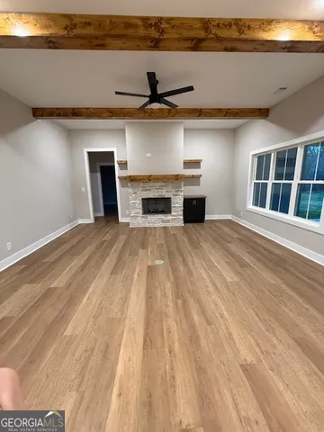 a view of an empty room with wooden floor and kitchen view