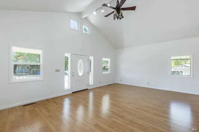 an empty room with wooden floor chandelier fan and windows