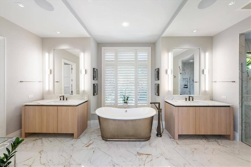 4220 Crayton Road Naples, FL 34103 - Photo 10 of 27 a bathroom with a tub a double vanity sink a mirror and a bathtub