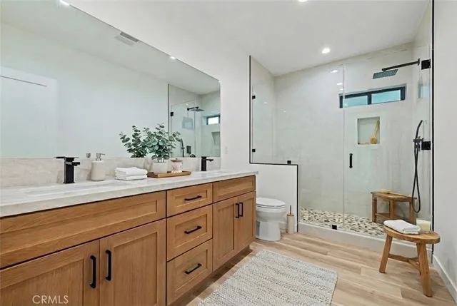 a spacious bathroom with double vanity a toilet a a mirror a lamp and a shower