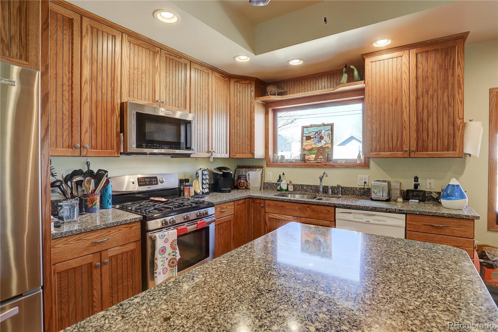 153 Park Avenue Fort Lupton, CO 80621 - Photo 9 of 35 a kitchen with kitchen island granite countertop a sink wooden cabinets and stainless steel appliances