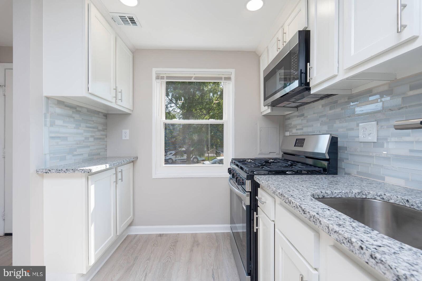 1842 Dutch Village Drive, Unit R264 Landover, MD 20785 - Photo 6 of 26 a kitchen with granite countertop a sink a stove a microwave and wooden cabinets