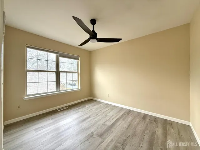 an empty room with wooden floor fan and windows