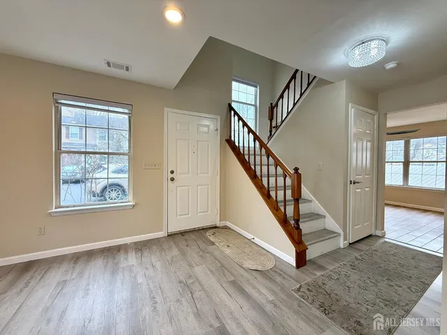 a view of an entryway with wooden floor leading to a furnished livingroom and windows