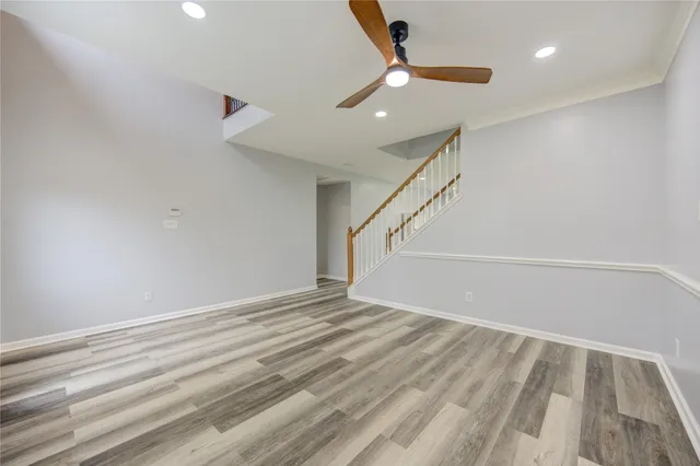 a view of an empty room with wooden floor and a ceiling fan