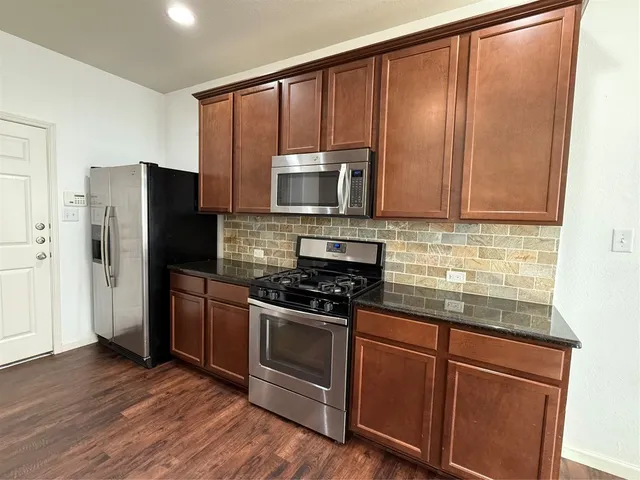 a kitchen with granite countertop wooden cabinets stainless steel appliances and a wooden floor