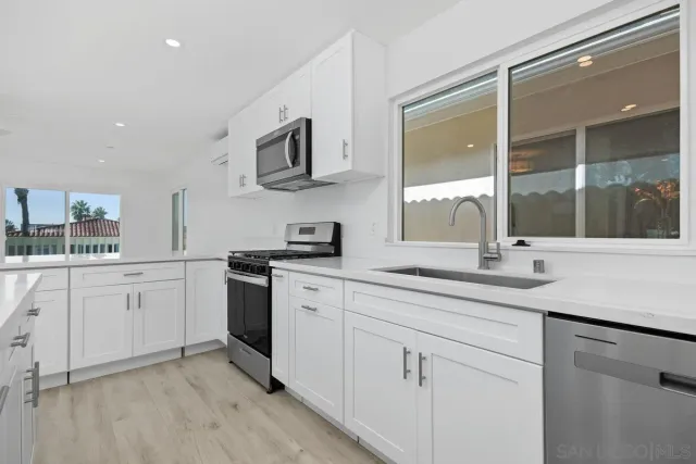 a kitchen with stainless steel appliances granite countertop white cabinets a sink and a window