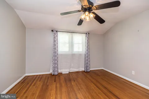an empty room with wooden floor chandelier fan and windows