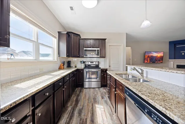 a kitchen with granite countertop stainless steel appliances a sink dishwasher a stove top oven a refrigerator with wooden cabinets