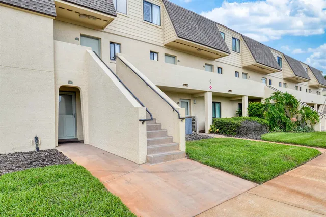 a view of a white house next to a yard with potted plants