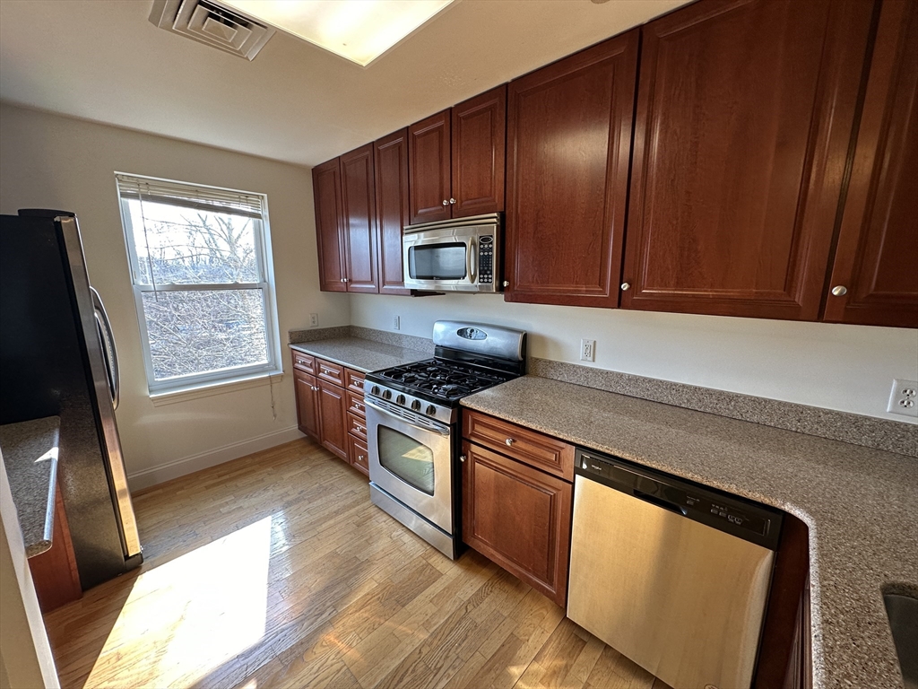 318 Rindge Avenue, Unit 216 Cambridge, MA 02140 - Photo 4 of 15 a kitchen with stainless steel appliances granite countertop wooden cabinets a stove a sink and a window