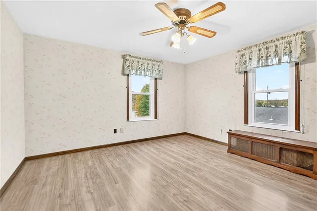 an empty room with wooden floor chandelier fan and windows