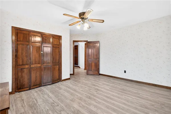 a view of an empty room with wooden floor and a ceiling fan