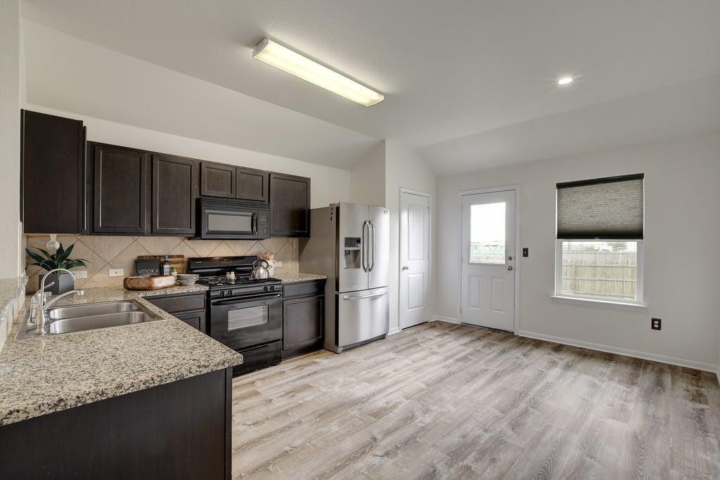 173 Rafe Court Kyle, TX 78640 - Photo 5 of 27 Kitchen with dark wood finish cabinetry, black appliances, vaulted ceiling, light stone counters, and decorative backsplash