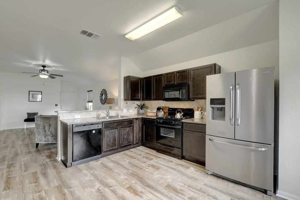 173 Rafe Court Kyle, TX 78640 - Photo 6 of 27 Kitchen featuring black appliances, dark wood finish cabinetry, lofted ceiling, a ceiling fan, and decorative backsplash