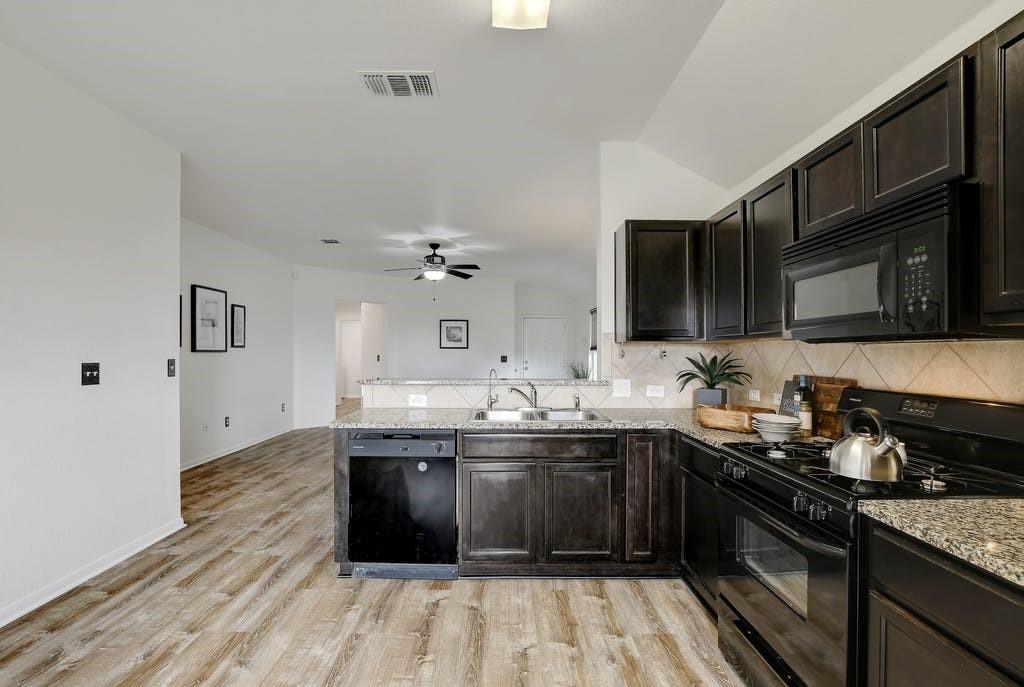173 Rafe Court Kyle, TX 78640 - Photo 7 of 27 Kitchen with black appliances, a peninsula, decorative backsplash, light wood-style flooring, and light stone counters