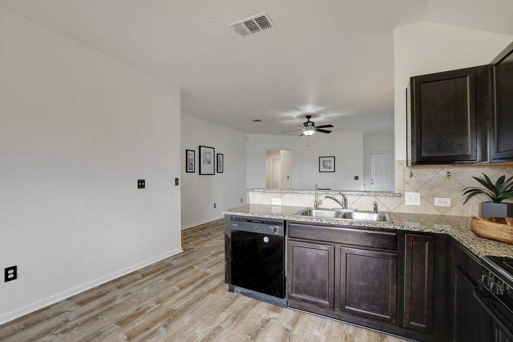 173 Rafe Court Kyle, TX 78640 - Photo 8 of 27 Kitchen featuring a peninsula, black appliances, dark wood finish cabinets, and light stone counters