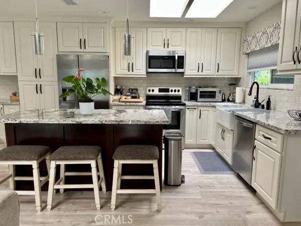 a kitchen with stainless steel appliances granite countertop a stove top oven a sink dishwasher and a refrigerator with wooden floor