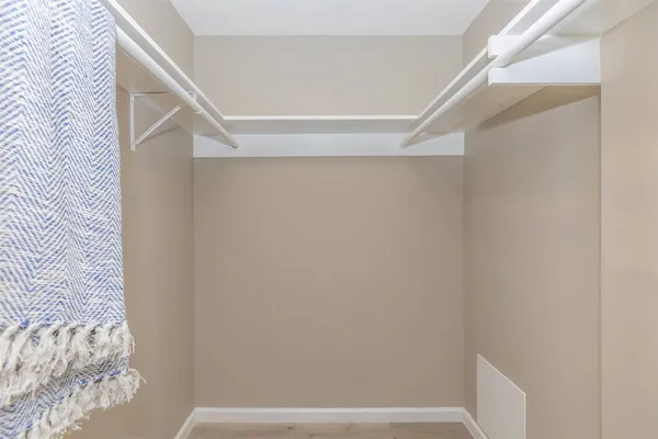 a bedroom with a bed and a lamp on dresser with wooden floor