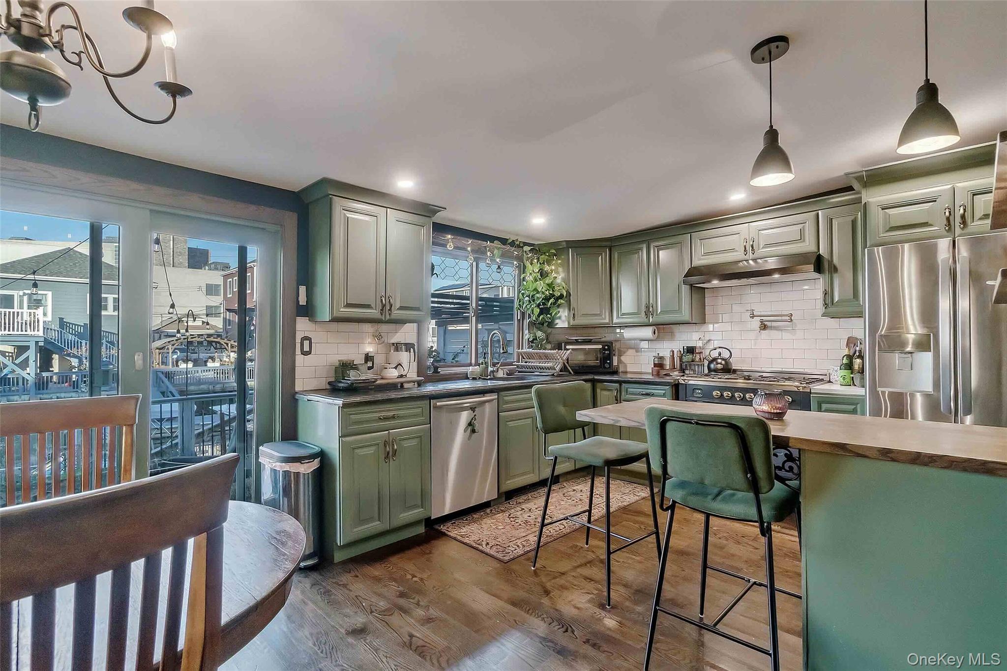 27 West 11th Road Queens, NY 11693 - Photo 9 of 18 Kitchen featuring green cabinetry, decorative light fixtures, stainless steel appliances, dark wood-style floors, and tasteful backsplash