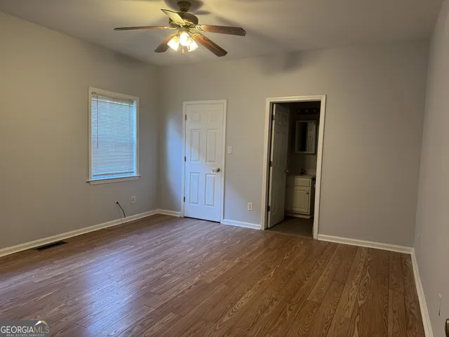 a view of an empty room with wooden floor and a ceiling fan