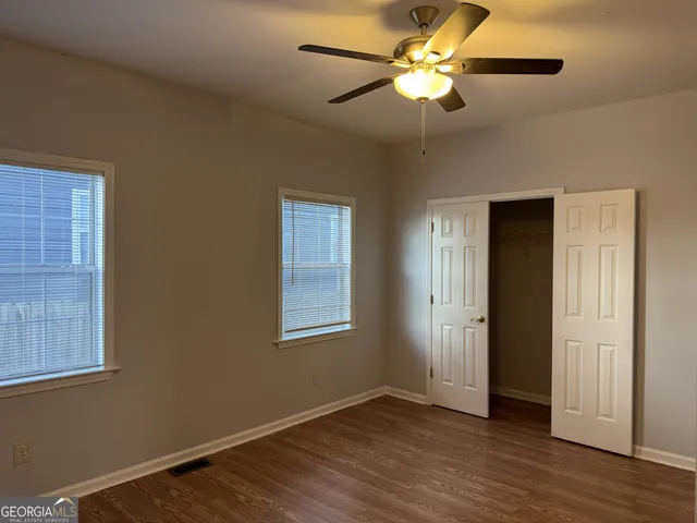 an empty room with wooden floor closet fan and windows