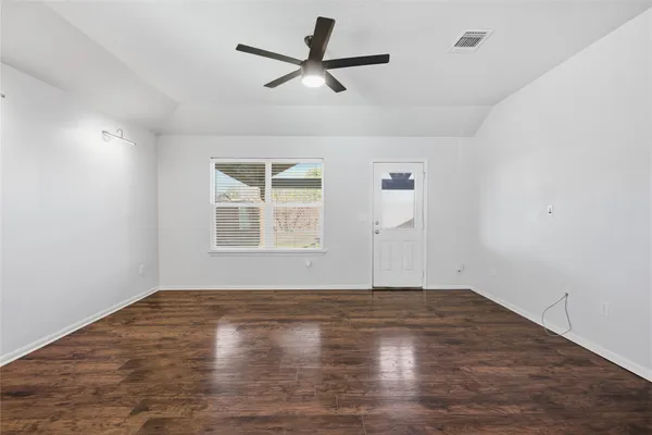 an empty room with wooden floor ceiling fan and windows