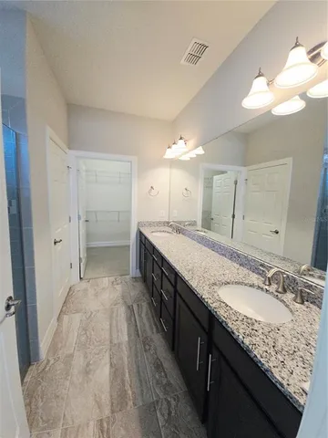 a spacious bathroom with a granite countertop double vanity sink a mirror and a shower