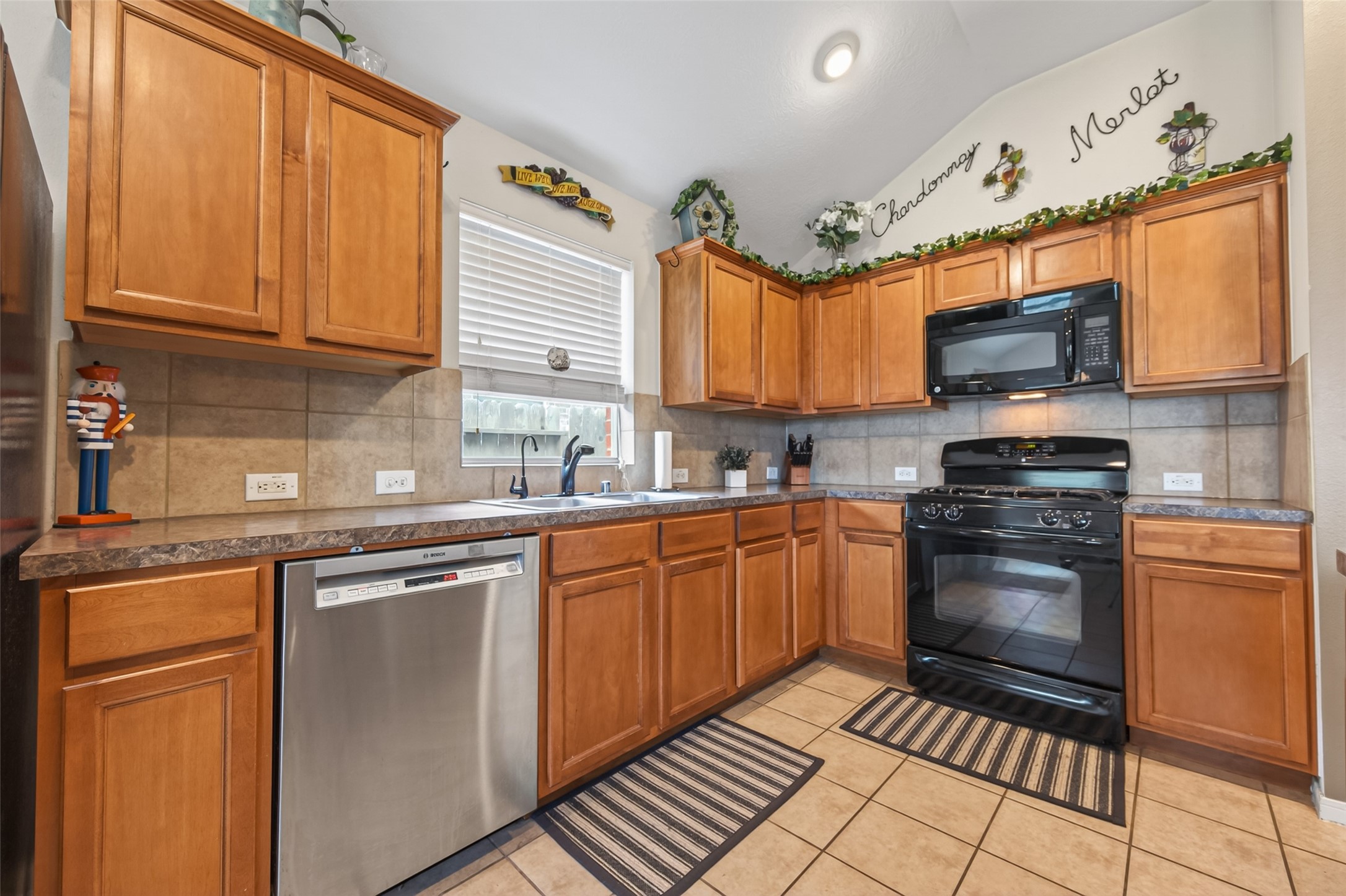 8622 Henrico Lane Rosenberg, TX 77469 - Photo 9 of 20 This kitchen features warm wooden cabinets, a sleek black stove and microwave, and a stainless steel dishwasher. The tiled backsplash and flooring complement the space, while decorative accents add charm. Bright and functional, it's ideal for home cooking.