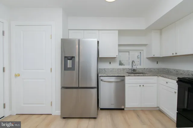 a kitchen with stainless steel appliances granite countertop a refrigerator a sink and white cabinets