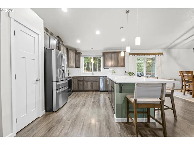 a kitchen with stainless steel appliances kitchen island granite countertop a refrigerator a sink a stove a dining table and chairs