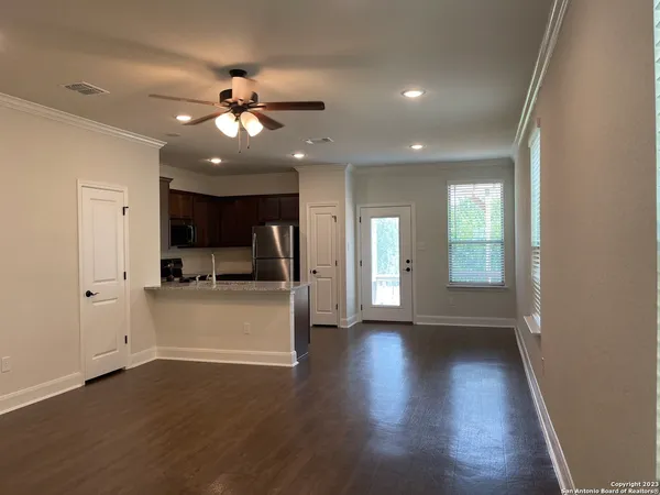 a view of an empty room and kitchen with wooden floor