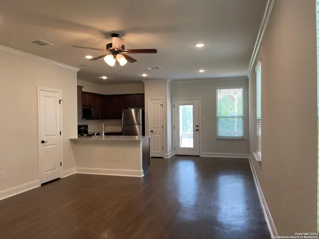 a view of an empty room and kitchen with wooden floor