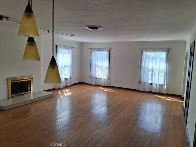 an empty room with wooden floor fireplace and windows
