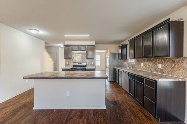 a large kitchen with stainless steel appliances granite countertop a large counter top and wooden floors