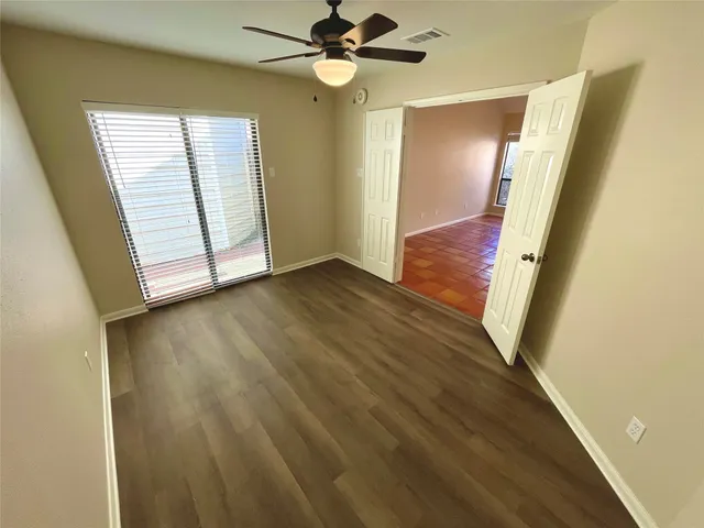 an empty room with wooden floor fan and windows