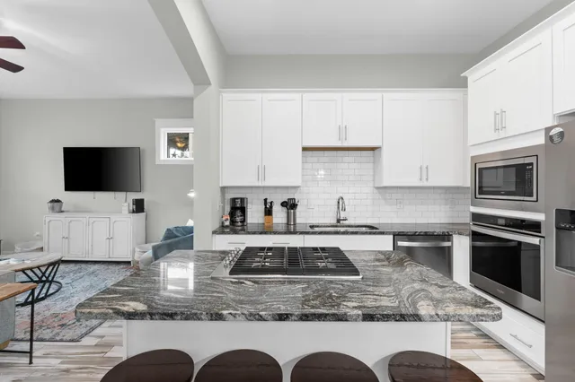 a kitchen with granite countertop a stove a sink dishwasher a dining table and chairs with wooden floor