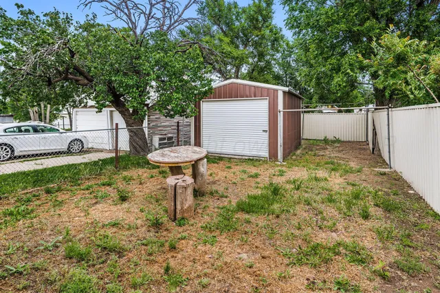 a backyard of a house with large trees and wooden fence