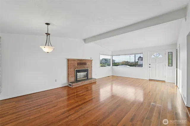 an empty room with wooden floor fireplace and windows