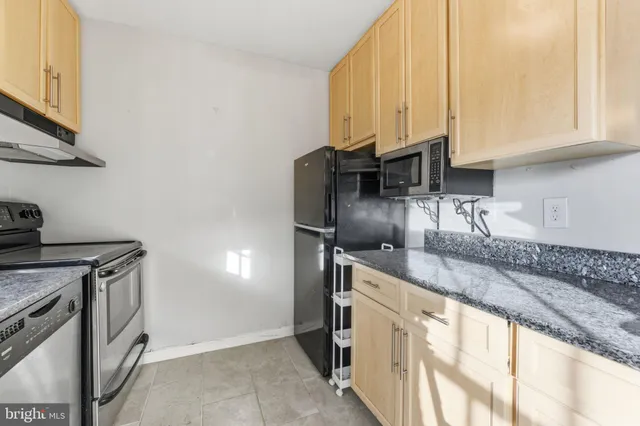 a kitchen with stainless steel appliances granite countertop a sink a stove and a refrigerator with wooden cabinets