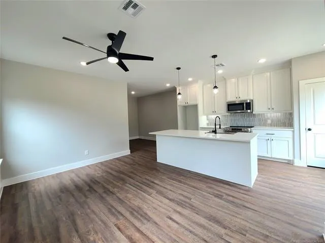 a large kitchen with stainless steel appliances kitchen island wooden floors and white walls
