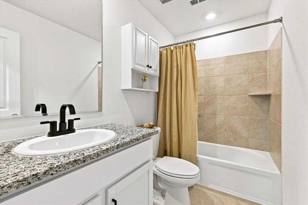 11741 Marcellus Way Rhome, TX 76078 - Photo 23 of 34 Granite-finish vanity countertop with an undermount sink and matte black faucet, white cabinetry, and tiled shower surround with an integrated niche