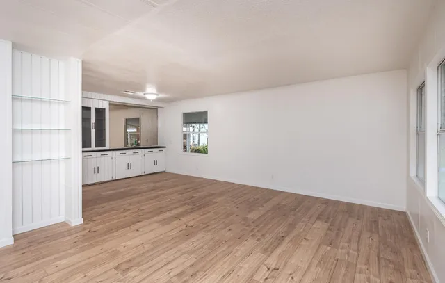 a view of empty room with wooden floor and kitchen view