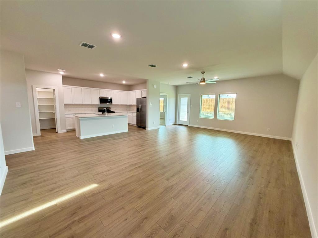 2203 Heatwave Lane Princeton, TX 75407 - Photo 3 of 32 a view of an empty room and kitchen with wooden floor