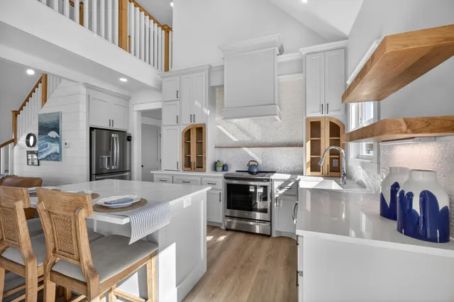 a large kitchen with stainless steel appliances kitchen island granite countertop a stove a sink a refrigerator and white cabinets with wooden floor
