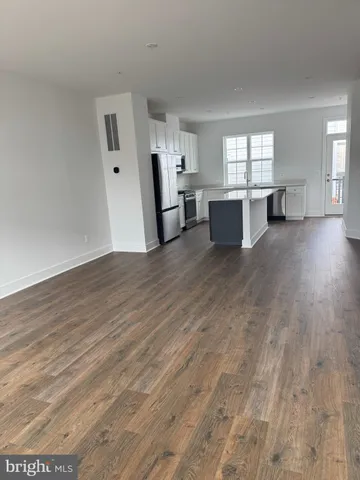 a view of a kitchen and an empty room with wooden floor and windows