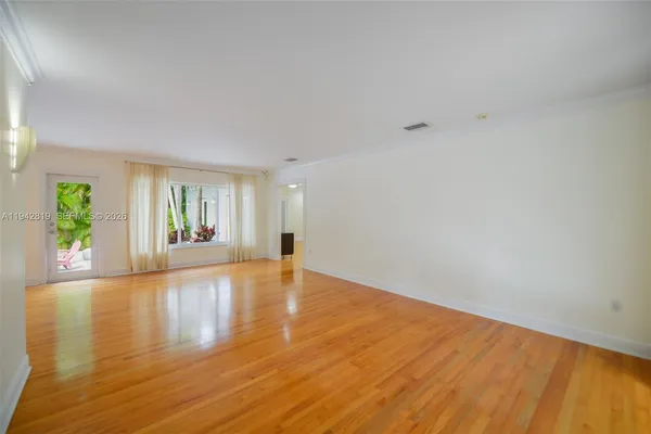 a view of an empty room with wooden floor and a window