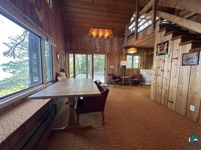 2763 Van Vac Road Ely, MN 55731 - Photo 4 of 37 Spacious room featuring extensive wood paneling, a full-height window overlooking exterior trees, an exposed wood beam ceiling, an open staircase with wood railings, and a glass sliding door providing outdoor access