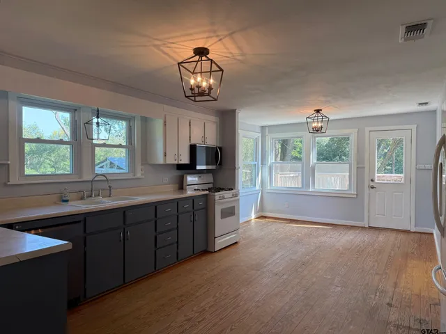 a kitchen with stainless steel appliances a dining table chairs refrigerator and microwave