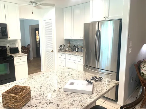 a kitchen with granite countertop a refrigerator a stove a sink dishwasher and white cabinets with wooden floor